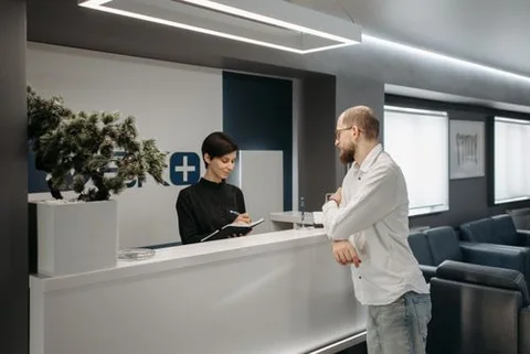Illustrative photo: staff welcoming a visitor at a reception desk.