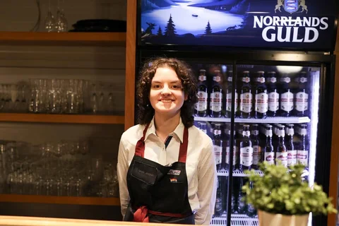 A person in an apron behind a bar.