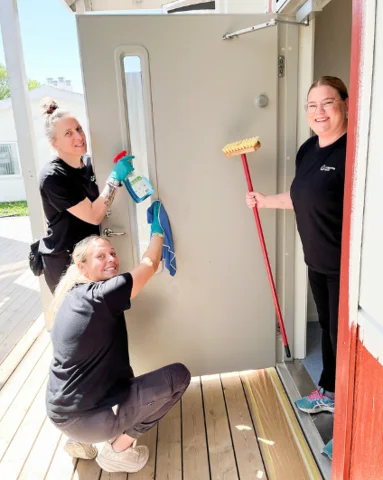 Three people cleaning a door and windows.